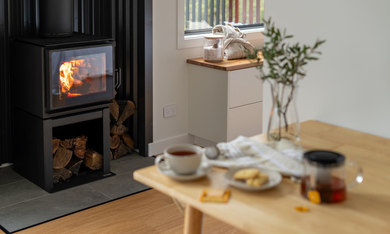 Wood fire burning beside a table set with tea inside a Breath cabin.