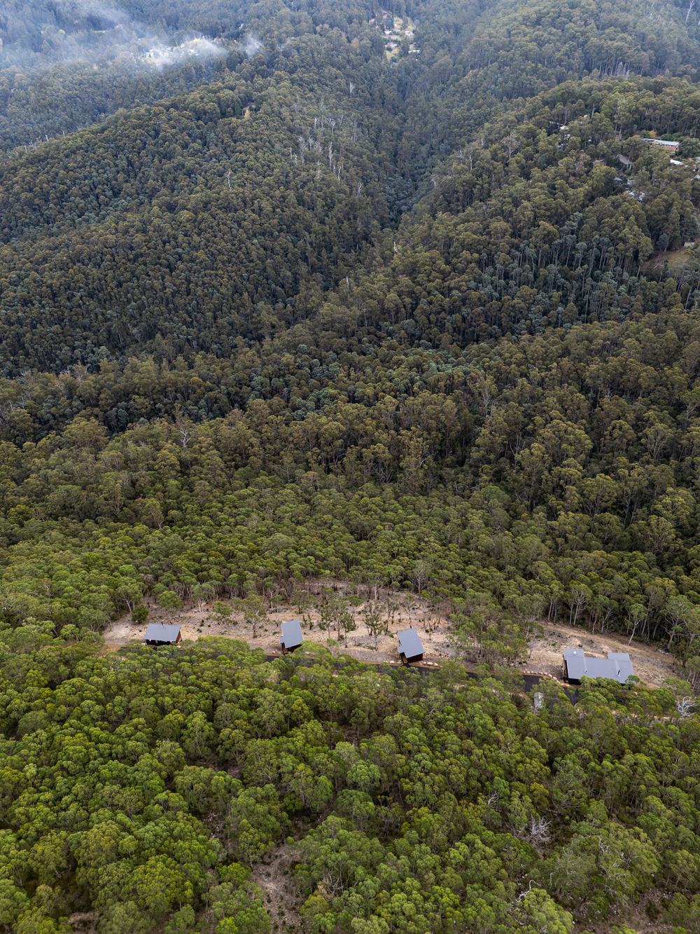Aerial shot of 3 hillside cabins in the forest kunanyi