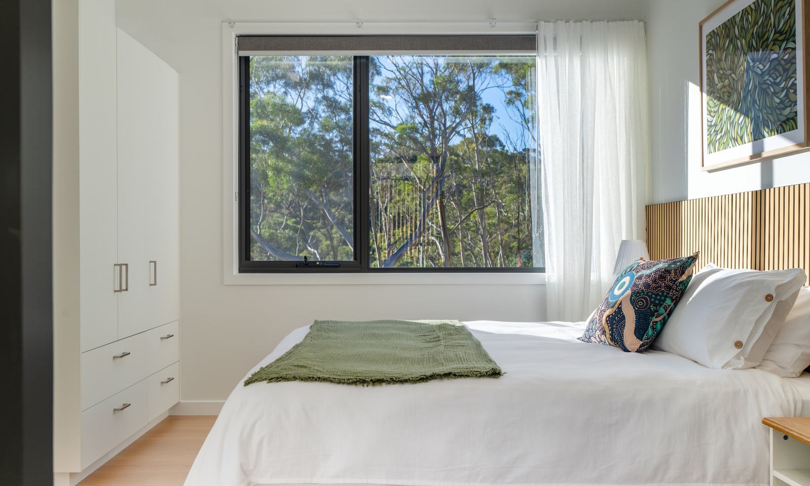 Bedroom of mosswood cabin with green design features looking out of window to forest