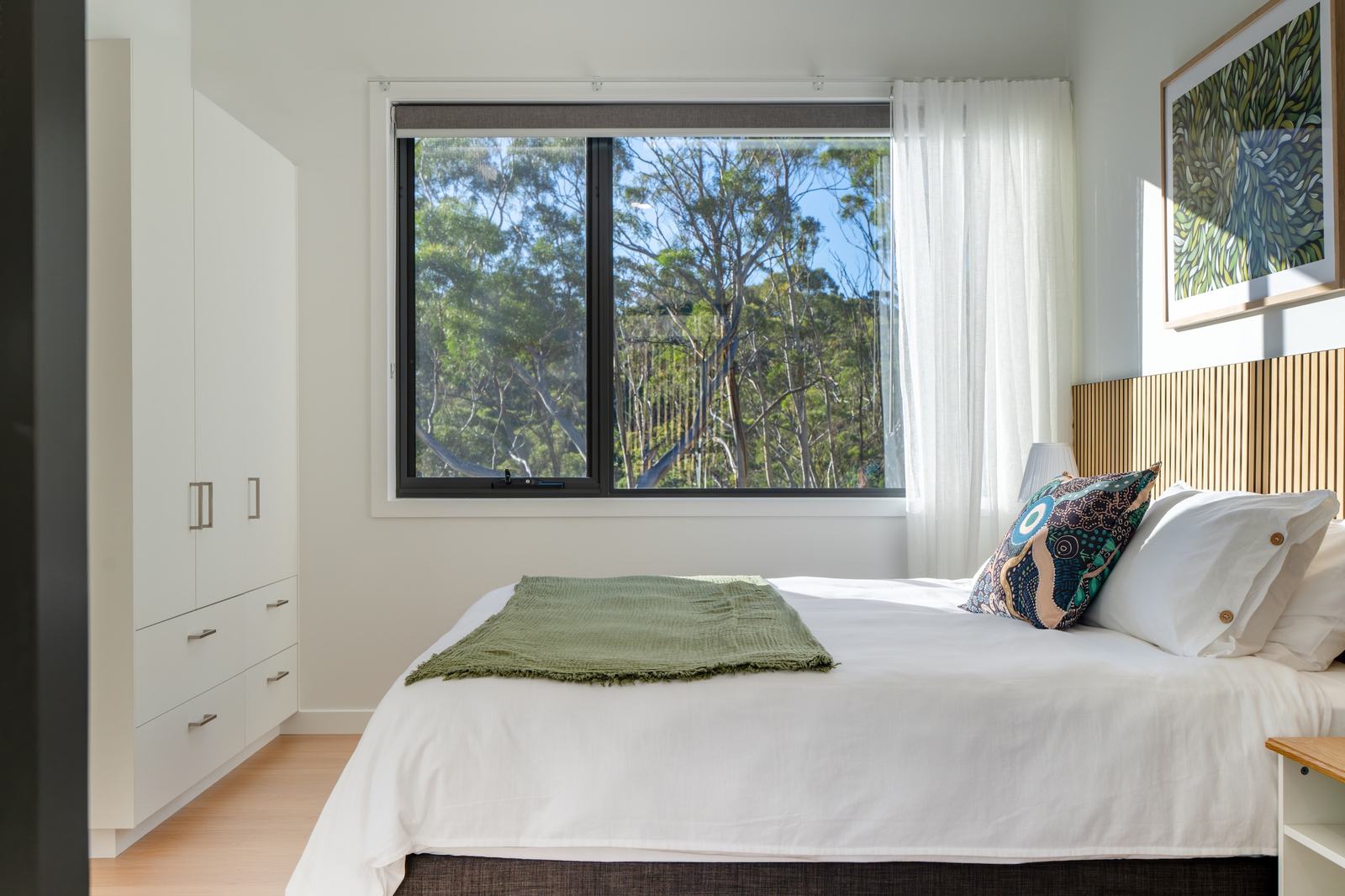 Bedroom of mosswood cabin with green design features looking out of window to forest