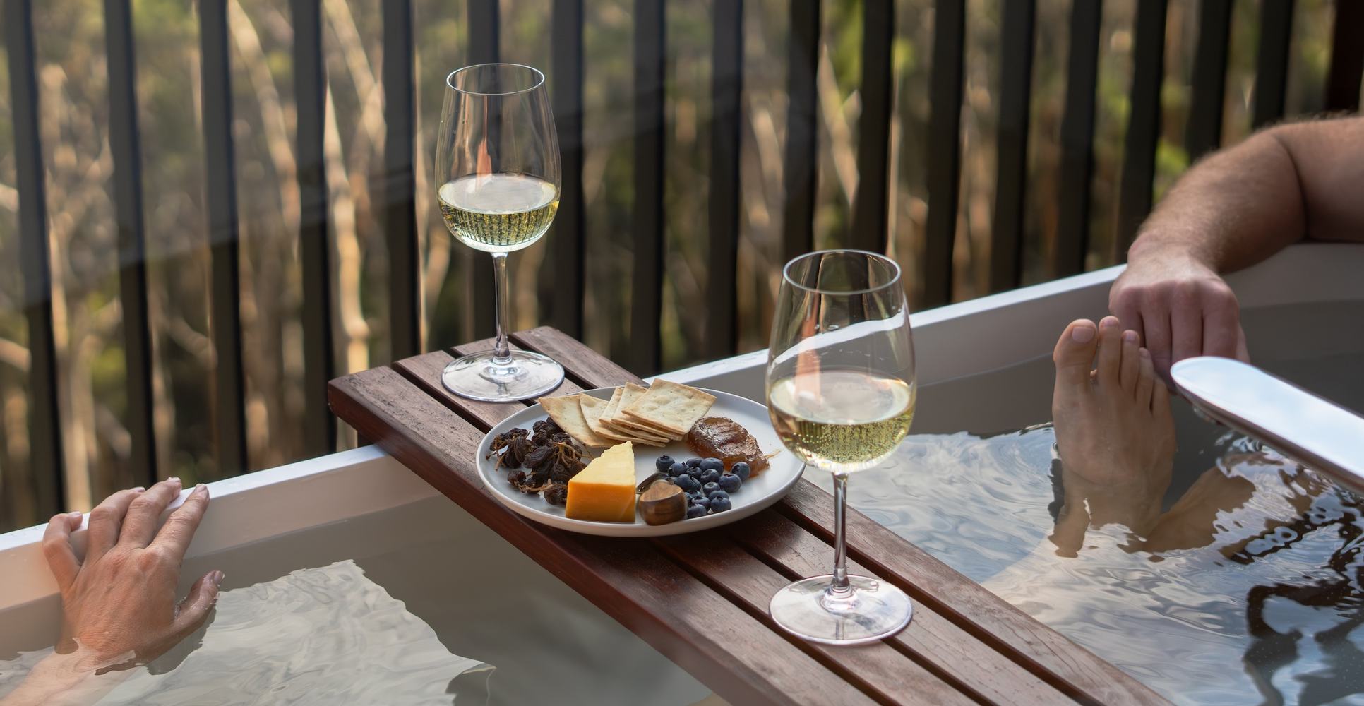 Two people in outdoor bath enjoying wine and cheese board